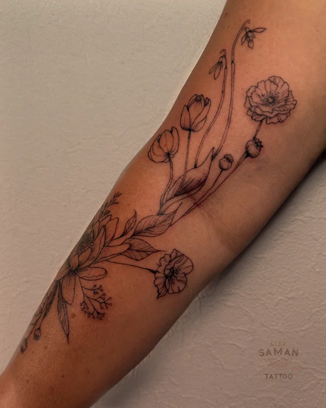 Tatouage de fleurs aux longues tiges et de feuillages fins sur l’avant-bras.