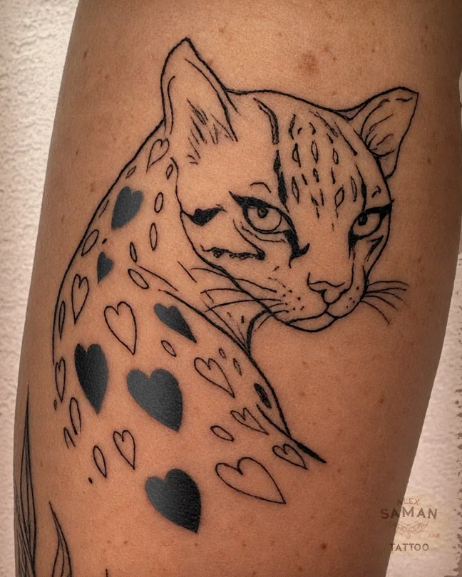 Tatouage d’une tête d’ocelot avec des taches en forme de cœurs et des détails en bleu.