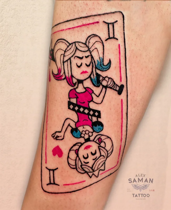 Tatouage d’une carte illustrée de Harley Quinn, avec des détails rouges, roses et bleus.