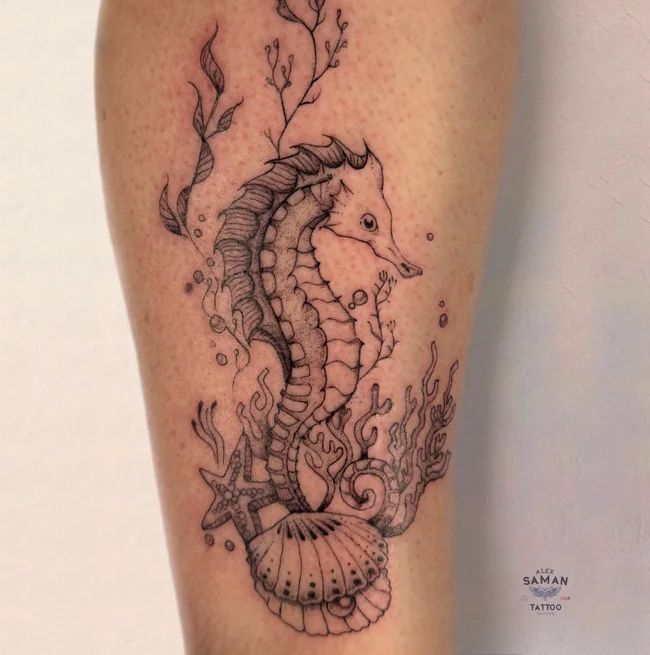 Tatouage d’un hippocampe entouré d’algues, avec un coquillage à sa base.