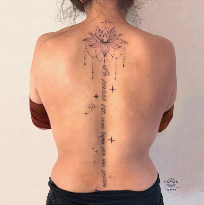 Tatouage d’un lotus entre les omoplates, prolongé par des ornements fins le long de la colonne vertébrale.