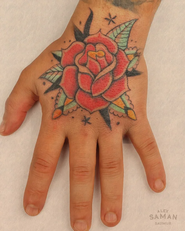 Tatouage d’une rose rouge en style old school aux feuilles vertes sur le dos de la main.