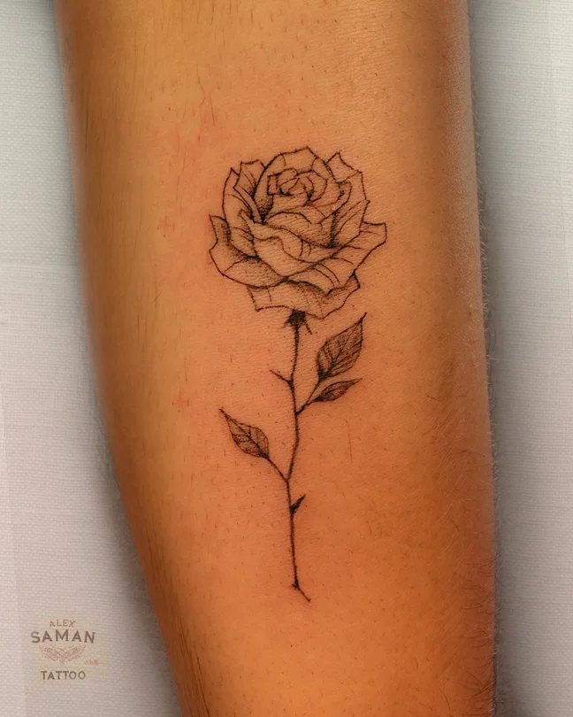 Tatouage d’une rose sur une longue tige fine, avec deux feuilles et de légers ombrages.