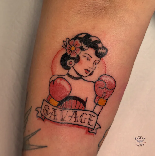 Tatouage d’une boxeuse illustrée avec des gants roses, une fleur dans les cheveux et le mot Savage.