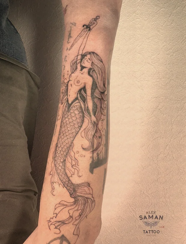 Tatouage d’une sirène aux longs cheveux tenant un trident, avec une queue détaillée.